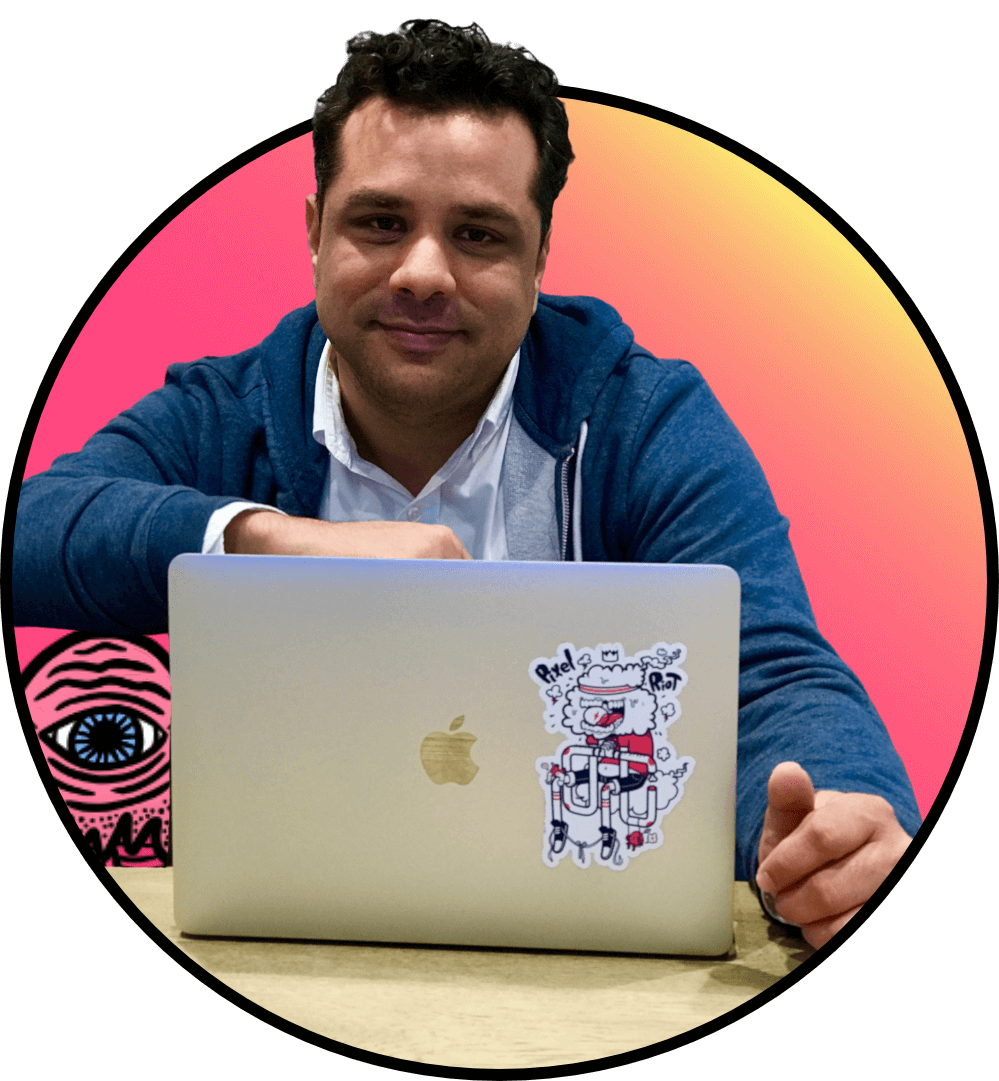 Photo of man Photo of man with brown hair wearing a blue hoodie and white button down shirt. He's sitting down and theres a laptop in front of him. Off to the side is an illustration of an alien and the man has his arm resting on it.with a hoodie and button down shirt. He's sitting down and theres a laptop in front of him. Off to the side is an illustration of an alien and the man has his arm resting on it.